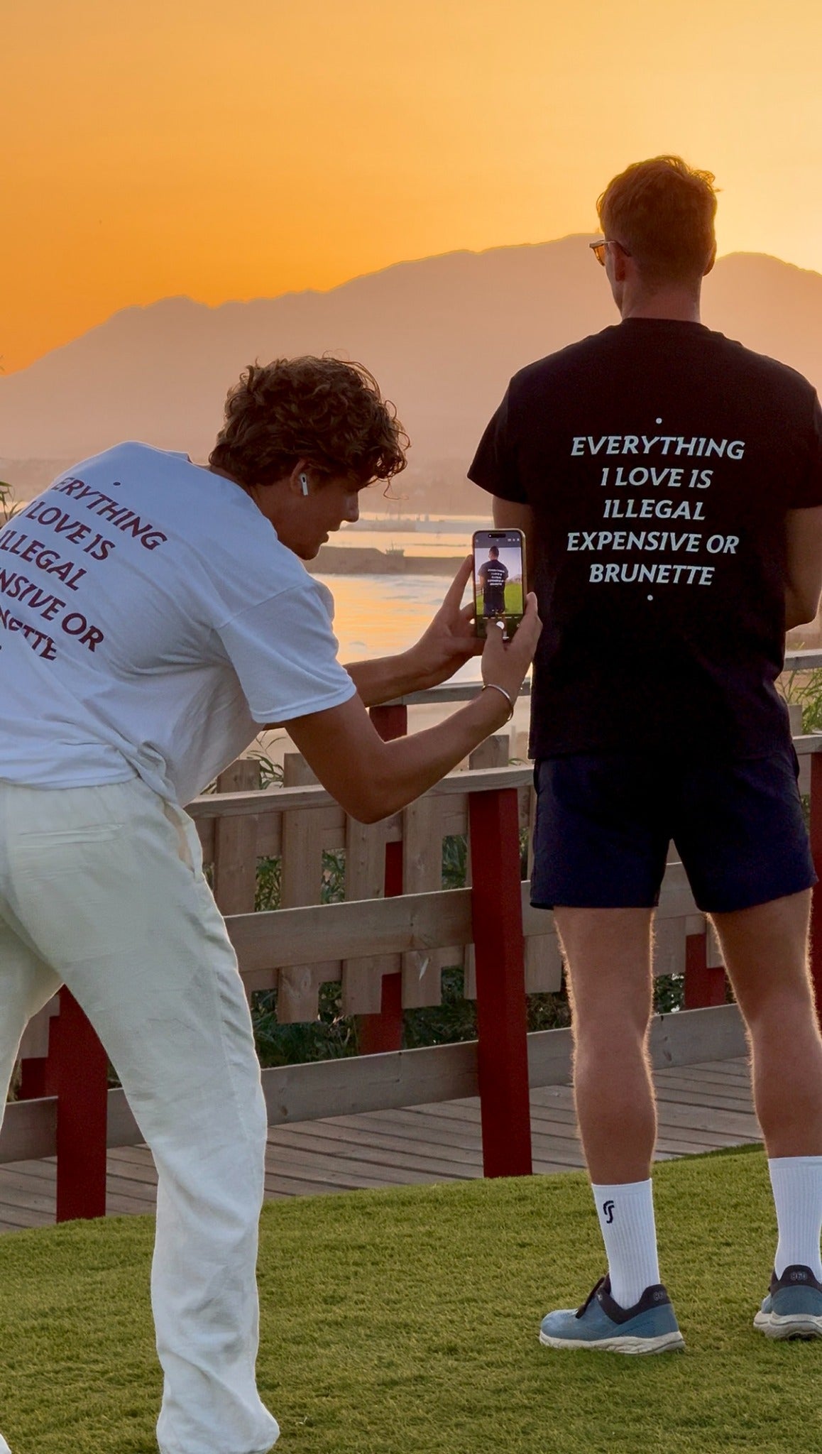 Two people wearing FRASED Everything I Love Is Illegal Expensive or Brunette tees during a sunset photoshoot