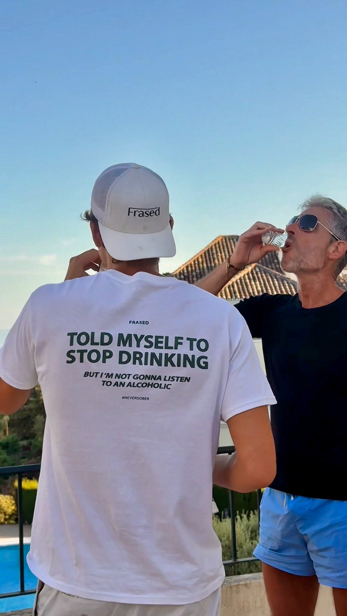 Person wearing a white FRASED Stop Drinking graphic tee outdoors beside a friend