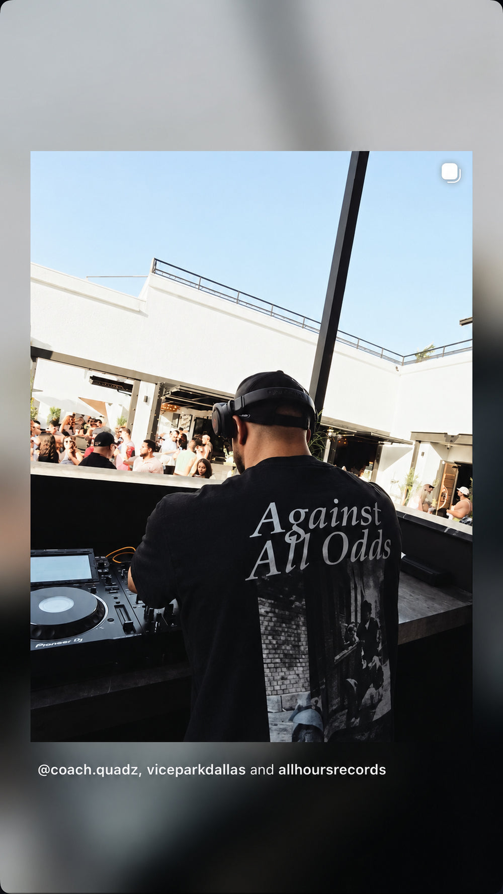 DJ spiller udendørs i sort FRASED T-shirt med 'Against All Odds' og grafisk rygtryk.