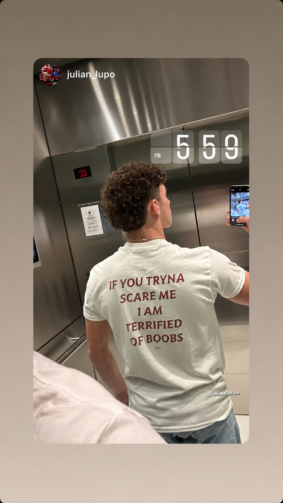 Mand i hvid IF YOU TRYNA SCARE ME, I AM TERRIFIED OF BOOBS T-shirt tager selfie i en elevator.