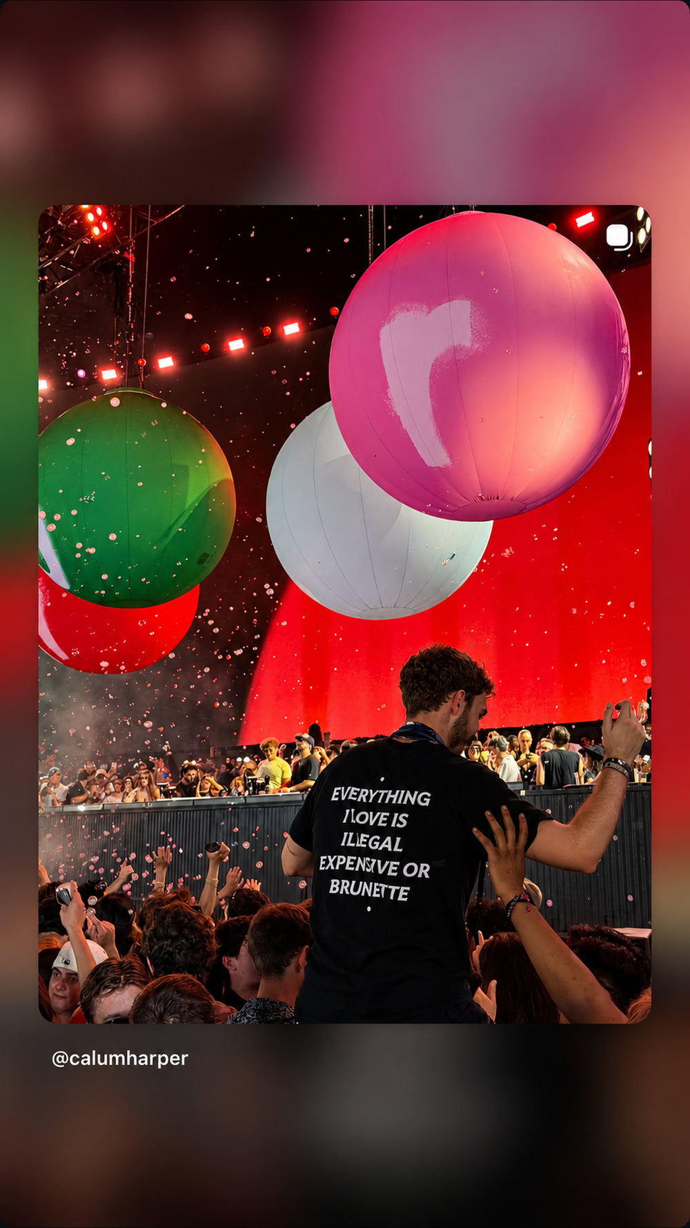 Mand i sort EVERYTHING I LOVE IS ILLEGAL, EXPENSIVE OR BRUNETTE T-shirt blandt store balloner og konfetti til koncert.
