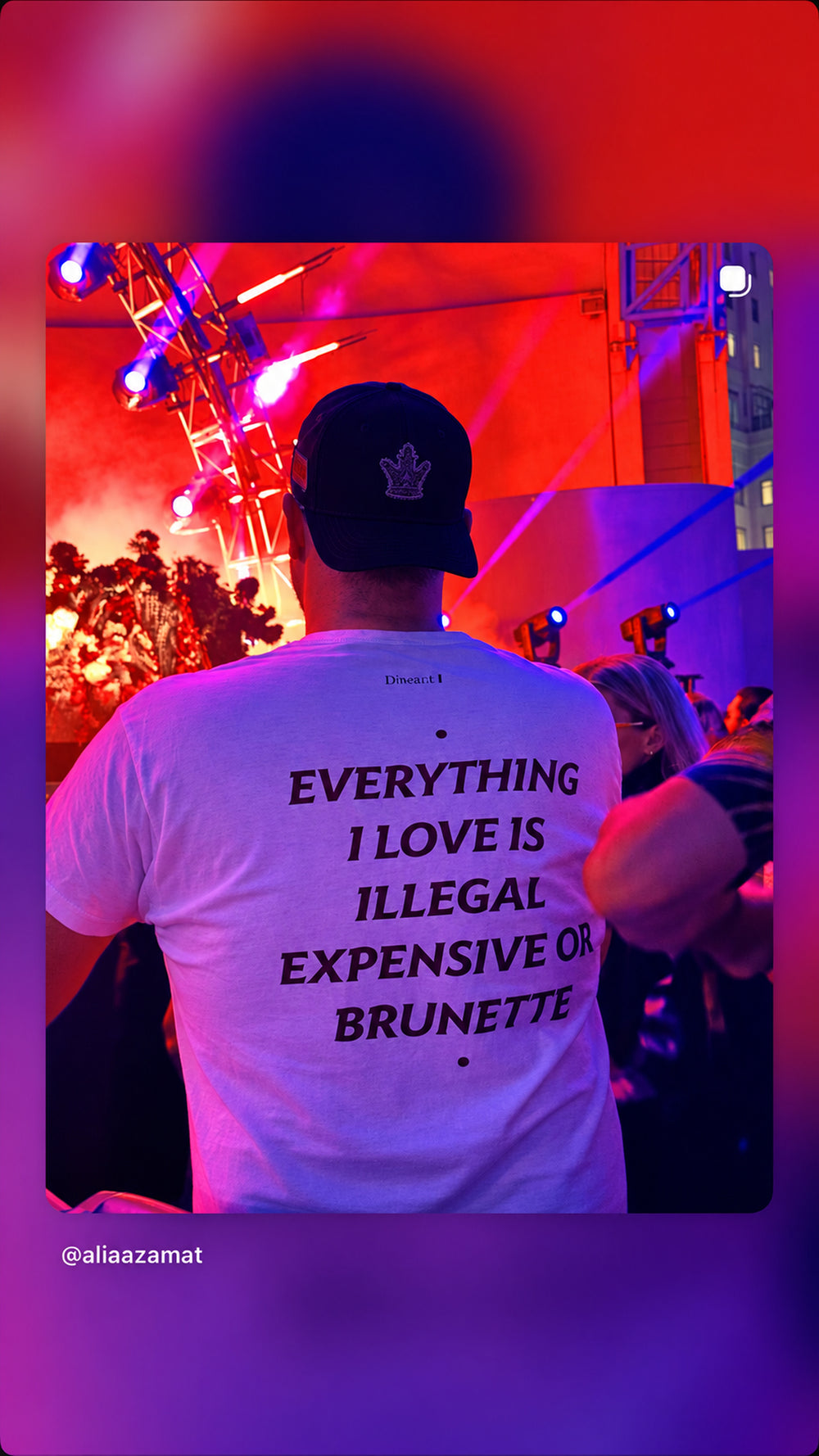 Person i hvid EVERYTHING I LOVE IS ILLEGAL, EXPENSIVE OR BRUNETTE T-shirt foran en scene i rødt og blåt lys.