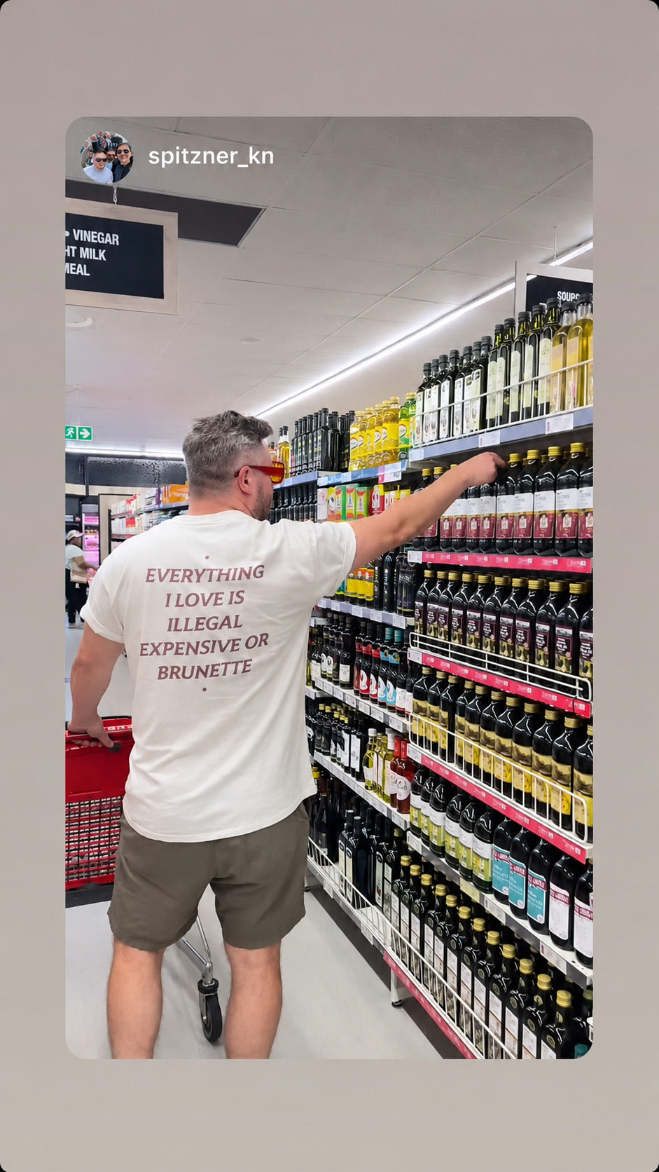 Mand i hvid EVERYTHING I LOVE IS ILLEGAL, EXPENSIVE OR BRUNETTE T-shirt handler i en butik.