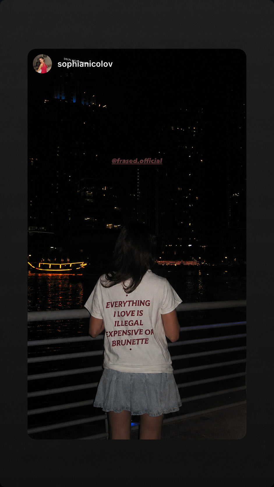Kvinde i hvid EVERYTHING I LOVE IS ILLEGAL, EXPENSIVE OR BRUNETTE T-shirt ser ud over vandet om aftenen.