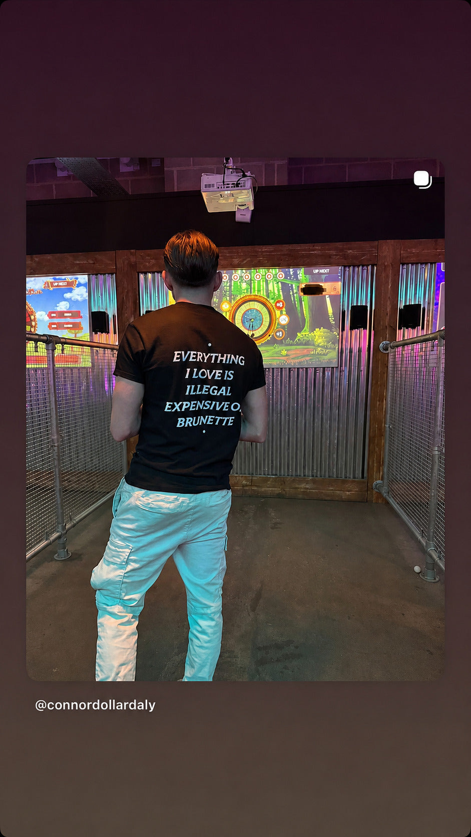 Mand i sort EVERYTHING I LOVE IS ILLEGAL, EXPENSIVE OR BRUNETTE T-shirt ved en spilleautomat.