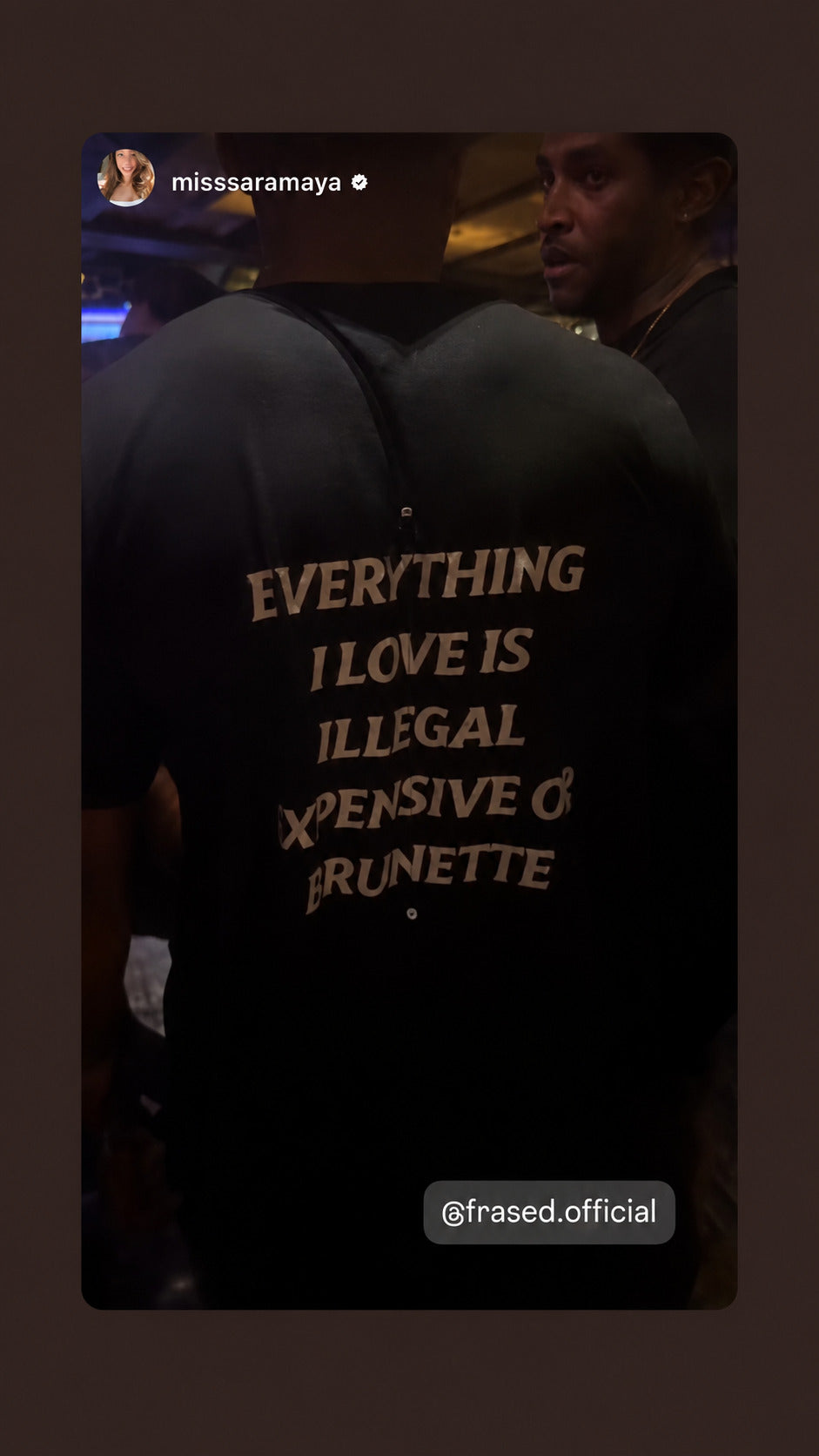 Nærbillede af sort EVERYTHING I LOVE IS ILLEGAL, EXPENSIVE OR BRUNETTE T-shirt i dæmpet belysning.