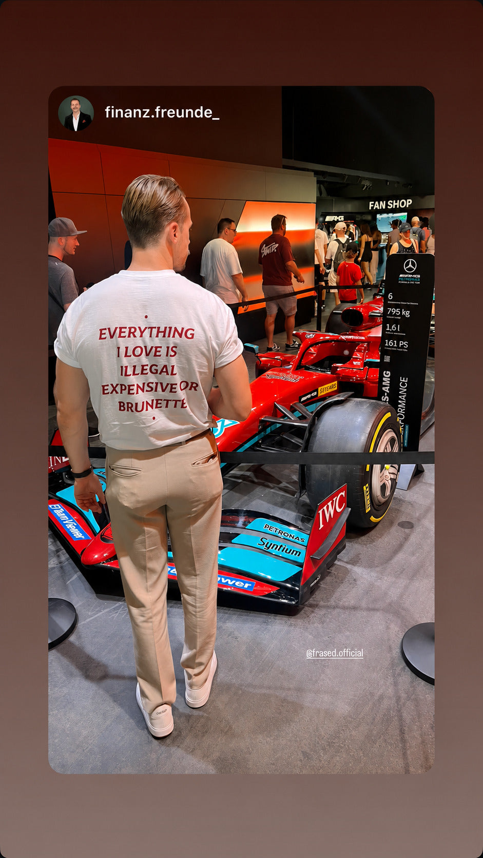 Mand i hvid EVERYTHING I LOVE IS ILLEGAL, EXPENSIVE OR BRUNETTE T-shirt ved en racerbil på en udstilling.