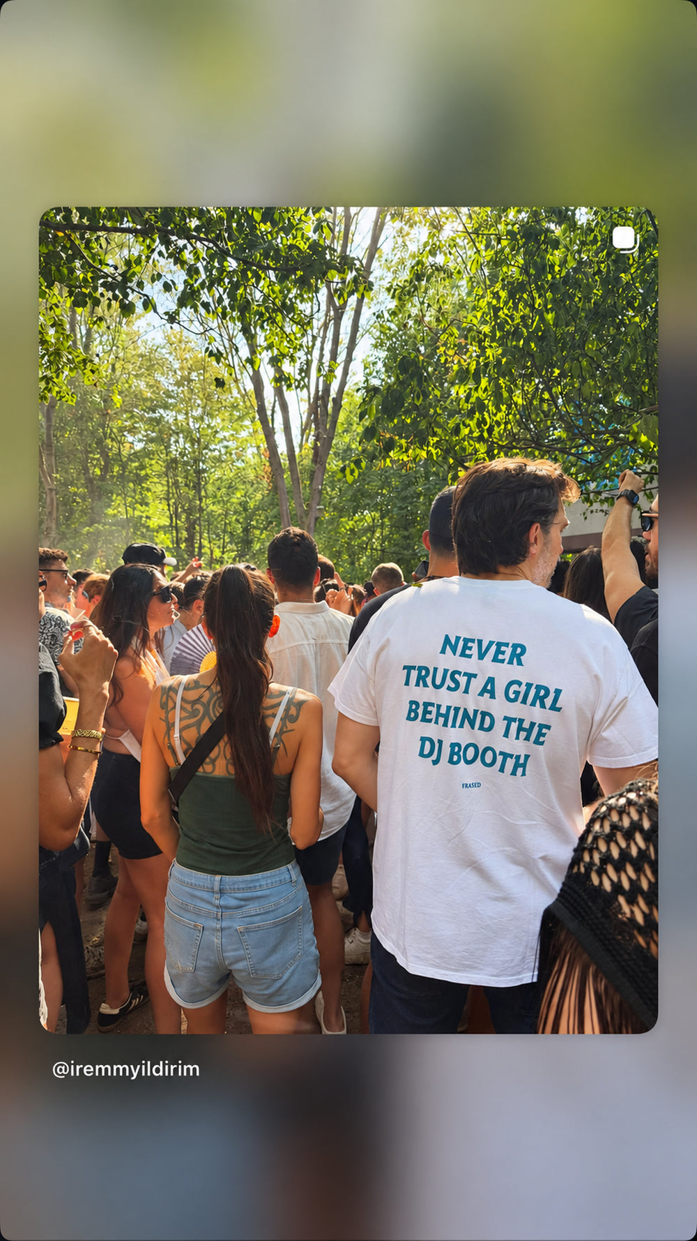 Mand i hvid NEVER TRUST A GIRL BEHIND THE DJ BOOTH T-shirt i publikum under træer