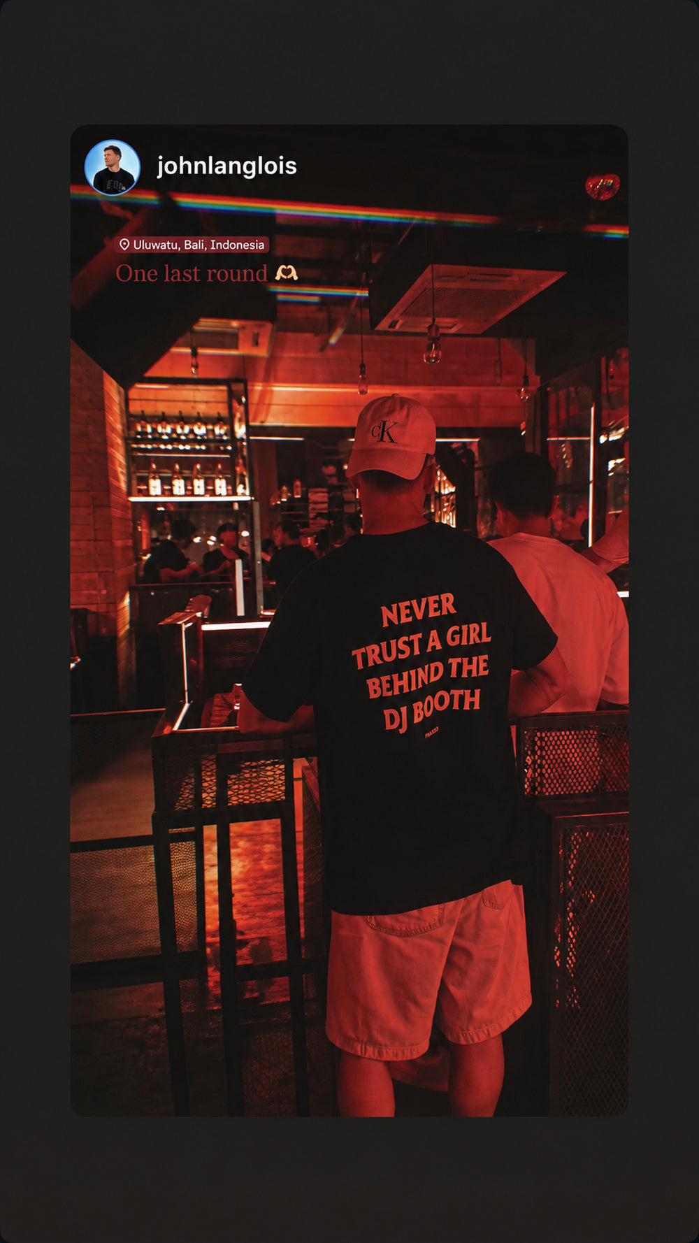 Mand i sort NEVER TRUST A GIRL BEHIND THE DJ BOOTH T-shirt i bar med rødt lys