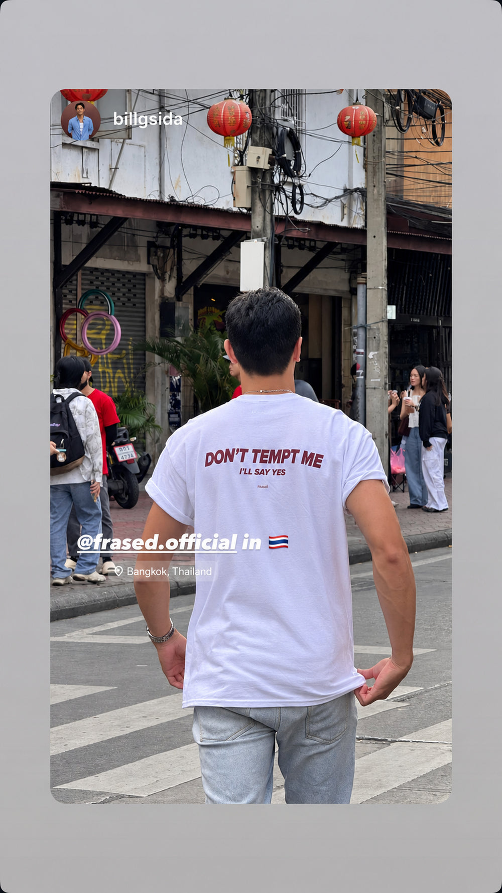 Man seen from behind at a pedestrian crossing in a white “DON’T TEMPT ME I’LL SAY YES” T-shirt.