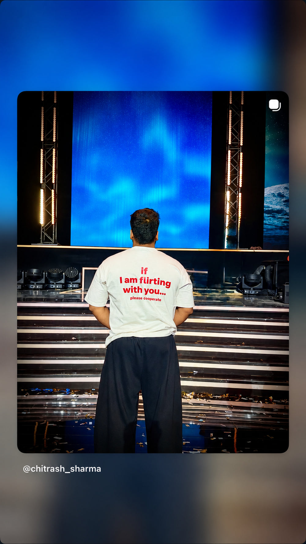 Mand i hvid IF I AM FLIRTING WITH YOU... PLEASE COOPERATE T-shirt foran en blåoplyst scene.