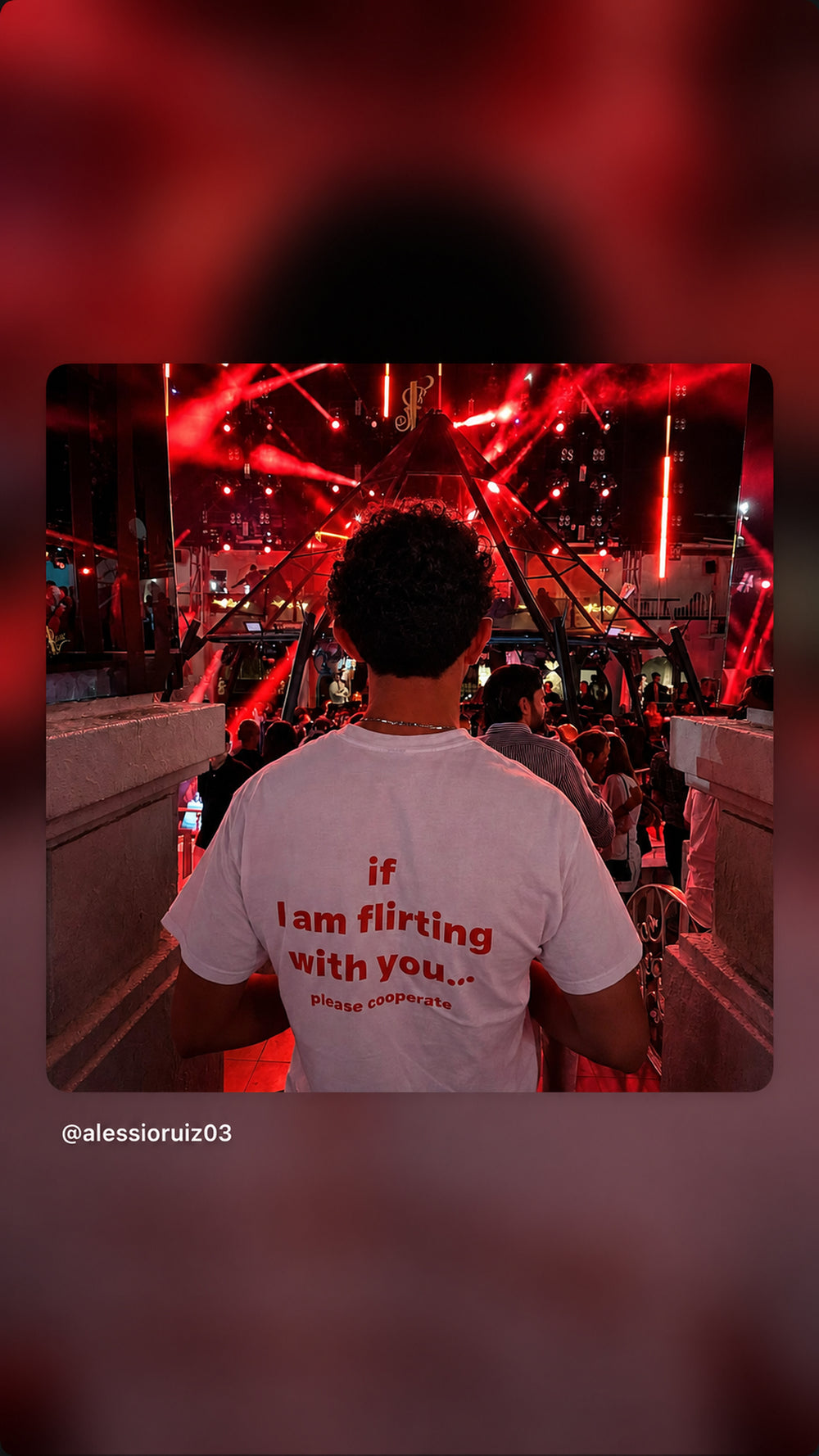 Person i hvid IF I AM FLIRTING WITH YOU... PLEASE COOPERATE T-shirt på en rødoplyst klub.