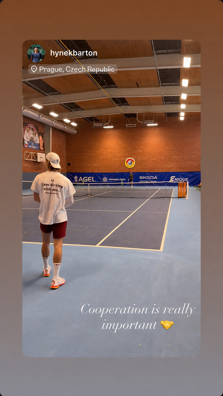 Person i hvid IF I AM FLIRTING WITH YOU... PLEASE COOPERATE T-shirt på en indendørs tennisbane.