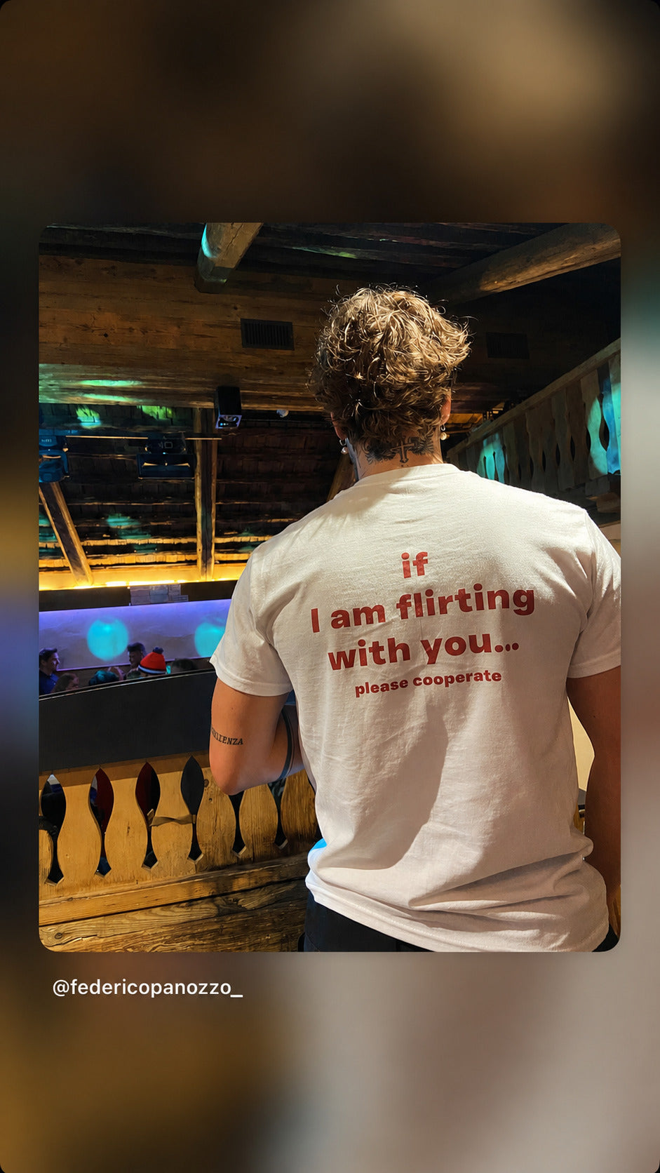 Mand set bagfra i hvid IF I AM FLIRTING WITH YOU... PLEASE COOPERATE T-shirt i en bar.