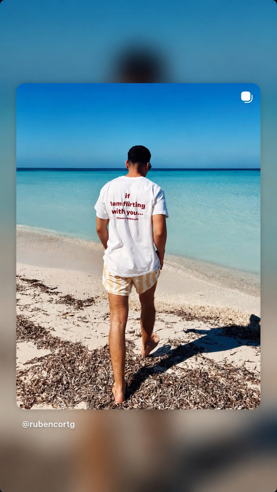 Mand set bagfra i hvid IF I AM FLIRTING WITH YOU... PLEASE COOPERATE T-shirt ved stranden.