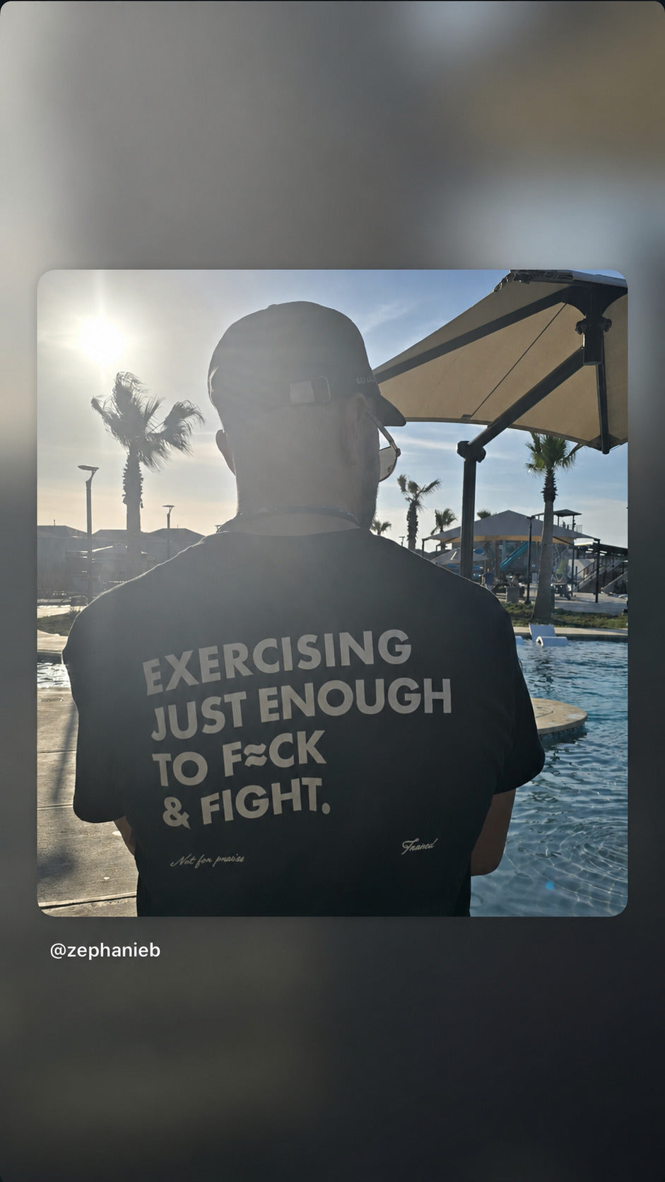 Man by a swimming pool in a black “EXERCISING JUST ENOUGH TO F*CK & FIGHT” T-shirt.