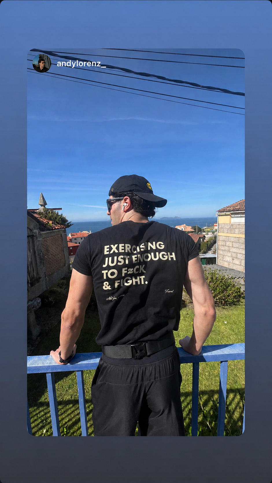 Man by a blue railing overlooking the sea in a black “EXERCISING JUST ENOUGH TO F*CK & FIGHT” T-shirt.