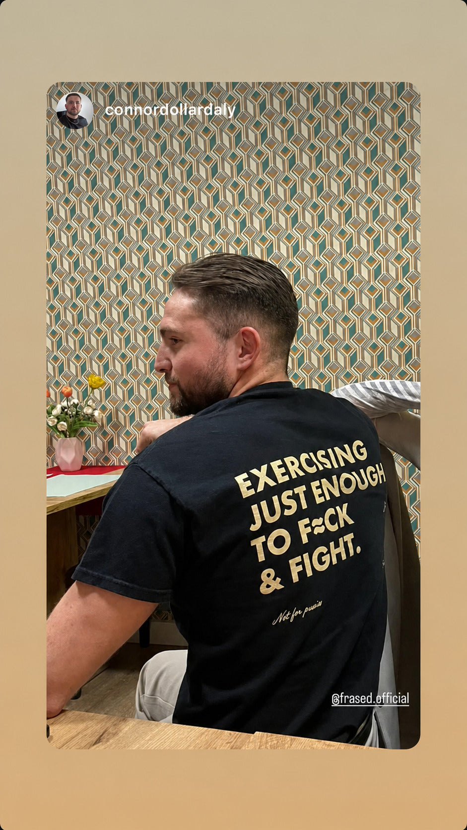 Man sitting at a table in a black “EXERCISING JUST ENOUGH TO F*CK & FIGHT” T-shirt.