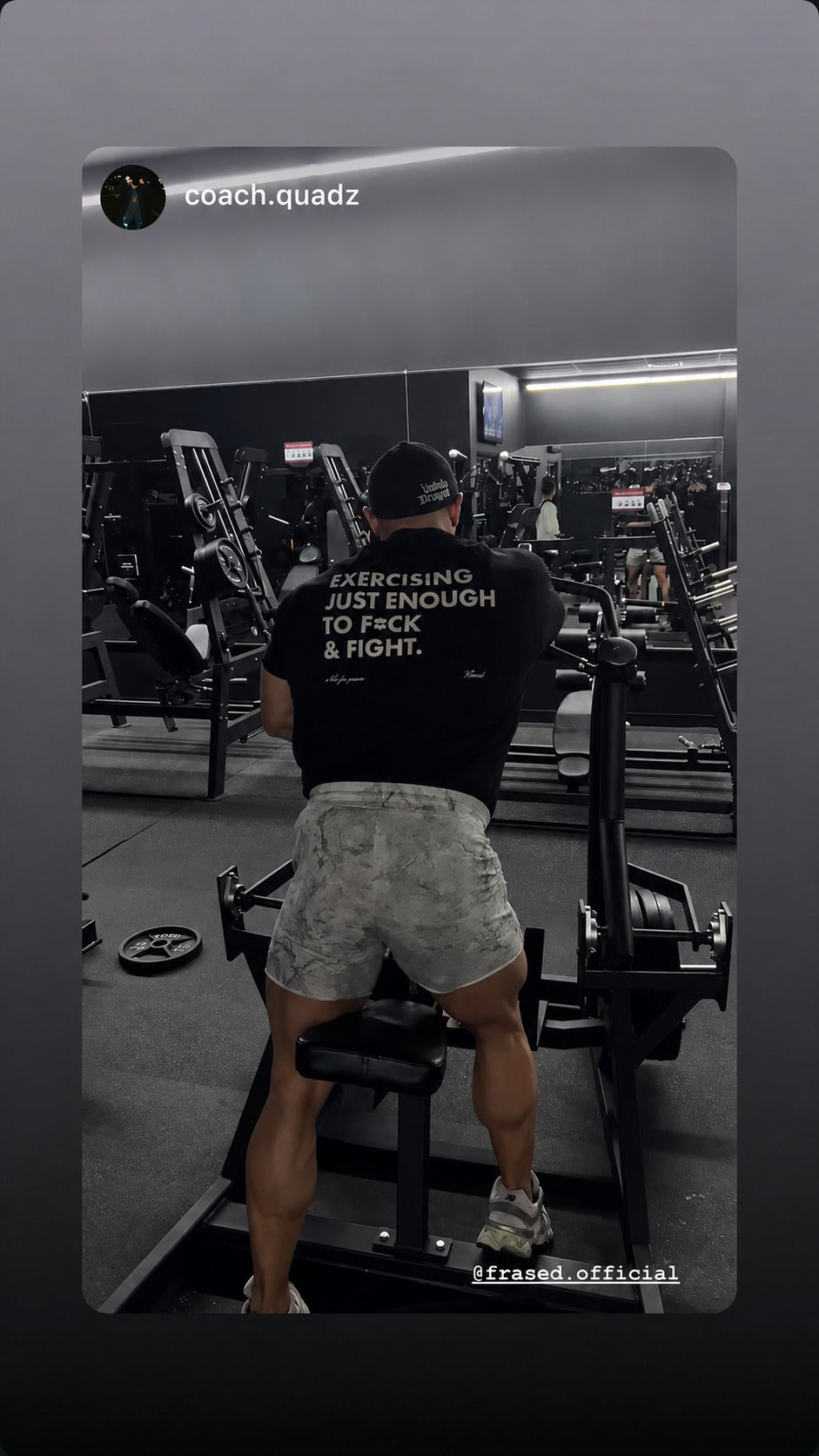 Man exercising on a gym machine in a black “EXERCISING JUST ENOUGH TO F*CK & FIGHT” T-shirt.
