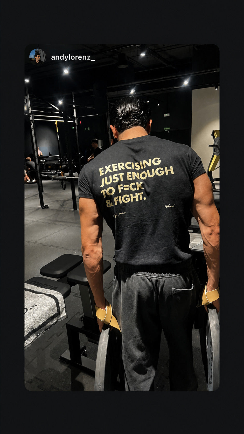 Man with weight plates at a gym wearing a black “EXERCISING JUST ENOUGH TO F*CK & FIGHT” T-shirt.