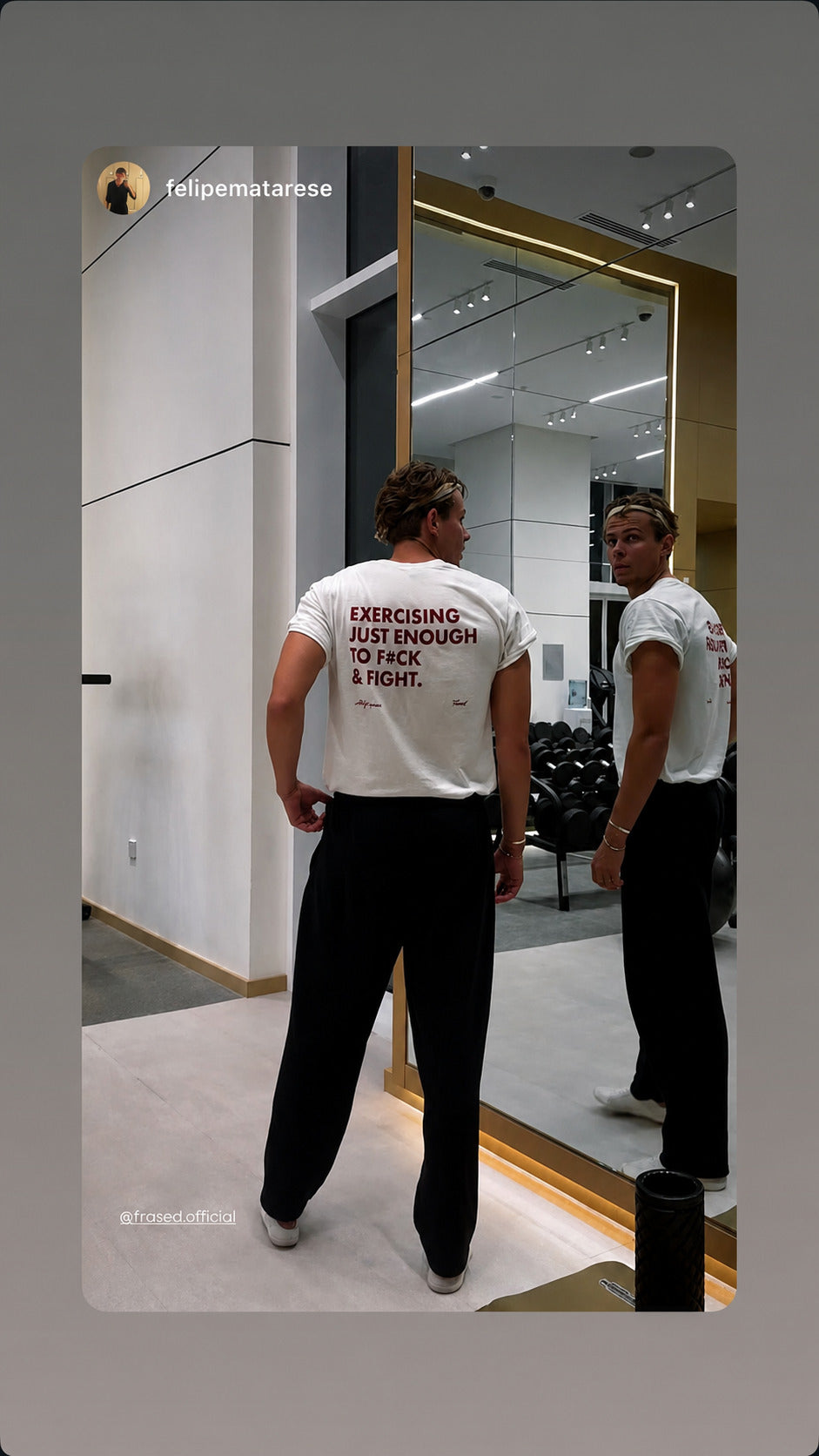 Man in a white “EXERCISING JUST ENOUGH TO F*CK & FIGHT” T-shirt in front of a gym mirror.