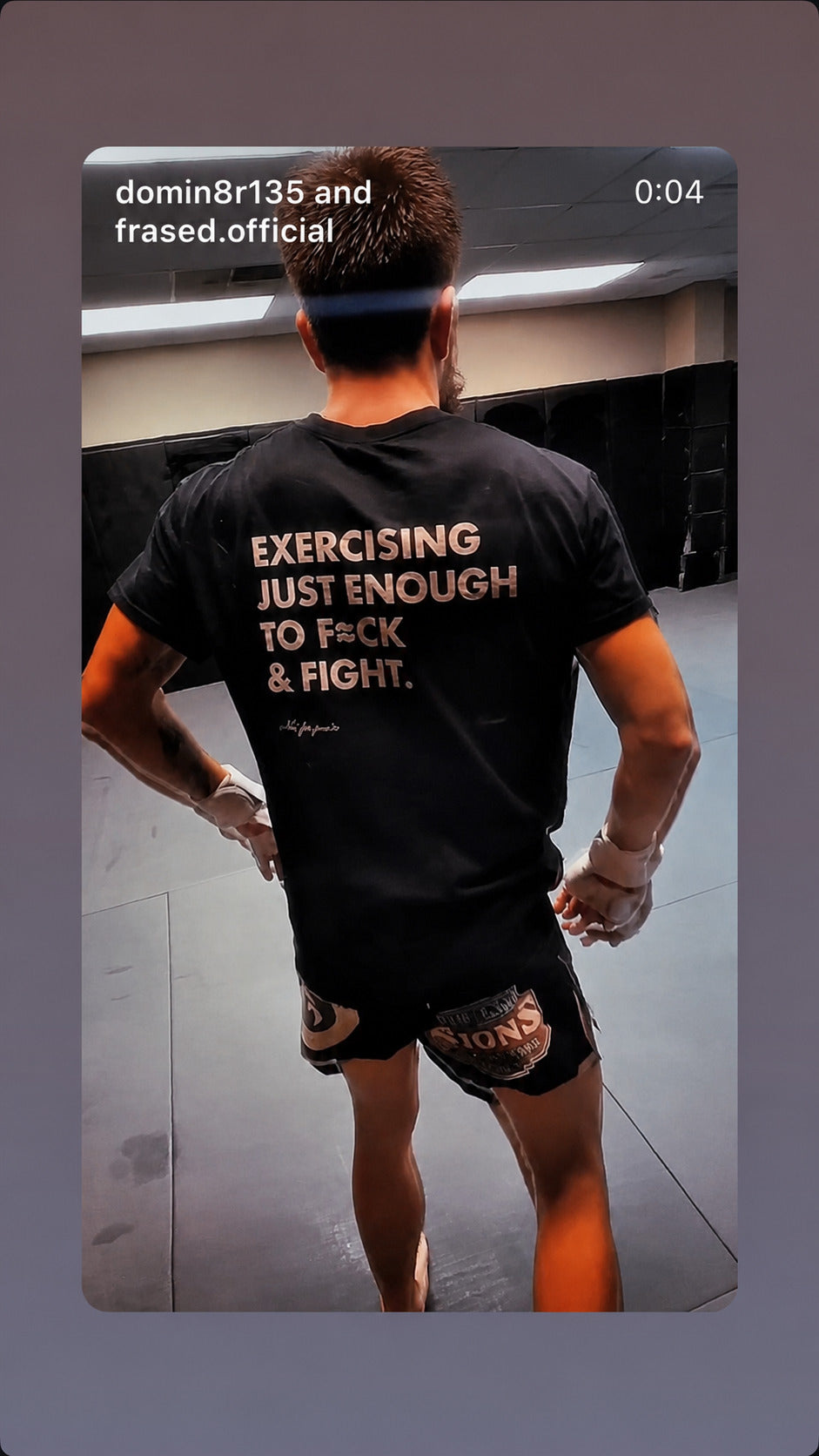 Martial artist seen from behind in a black “EXERCISING JUST ENOUGH TO F*CK & FIGHT” T-shirt.