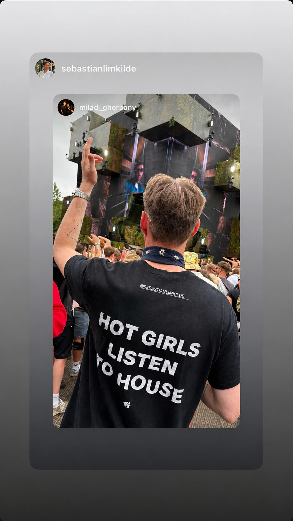 Man seen from behind in front of a festival stage wearing a black “HOT GIRLS LISTEN TO HOUSE” T-shirt.