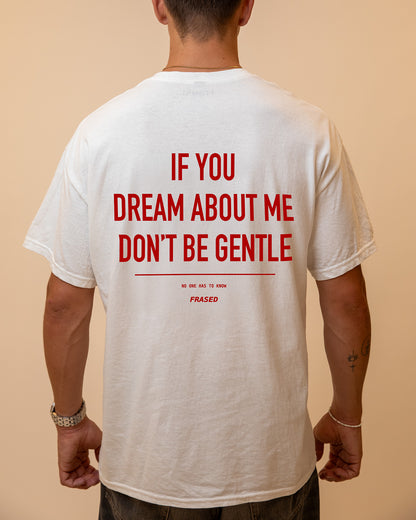 A man viewed from behind wearing a white t-shirt with bold red text on the back that reads 'IF YOU DREAM ABOUT ME DON'T BE GENTLE' and smaller text below reading 'NO ONE HAS TO KNOW PHASED'.