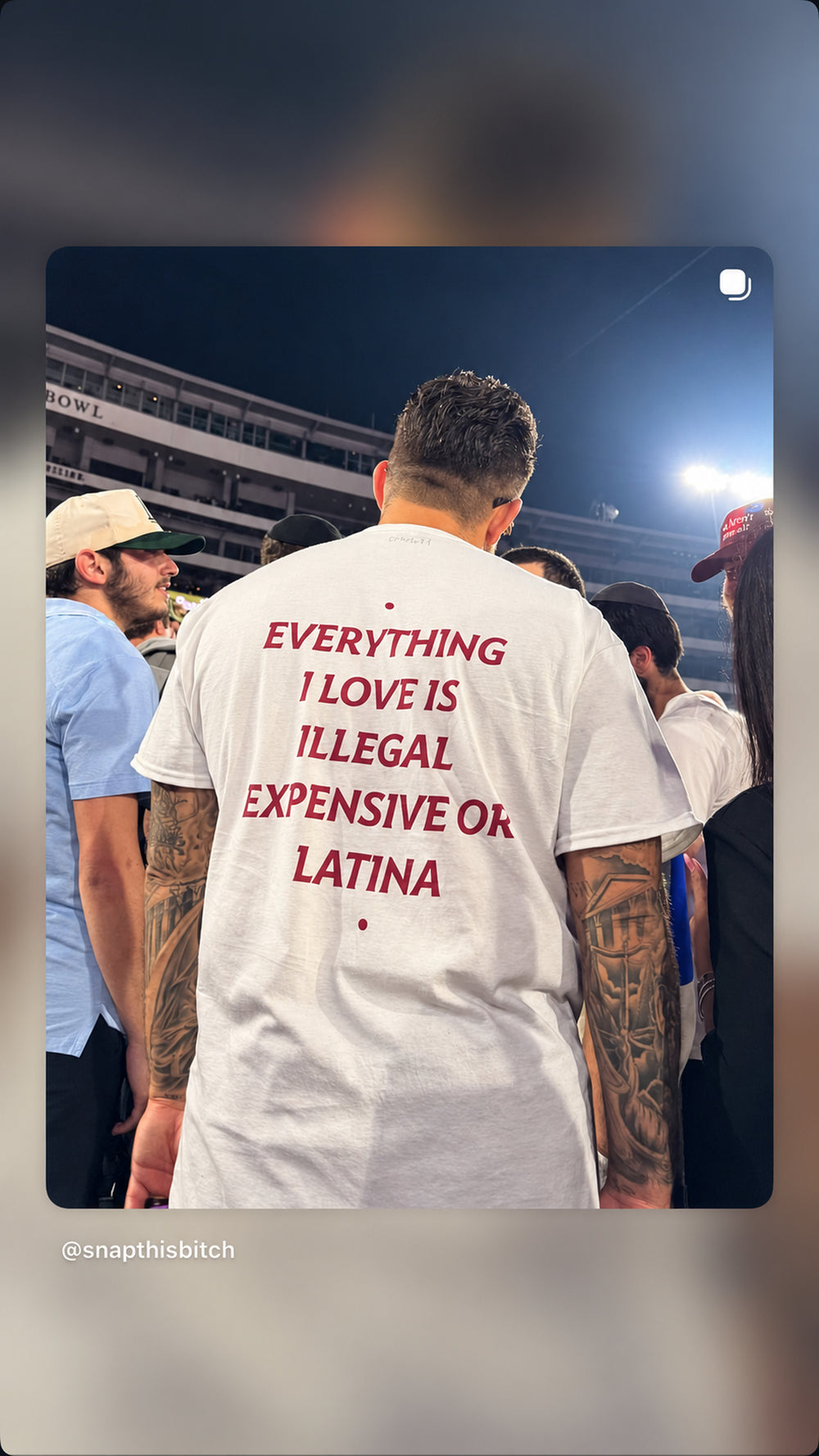 Mand i hvid EVERYTHING I LOVE IS ILLEGAL, EXPENSIVE OR LATINA T-shirt i en menneskemængde om aftenen.