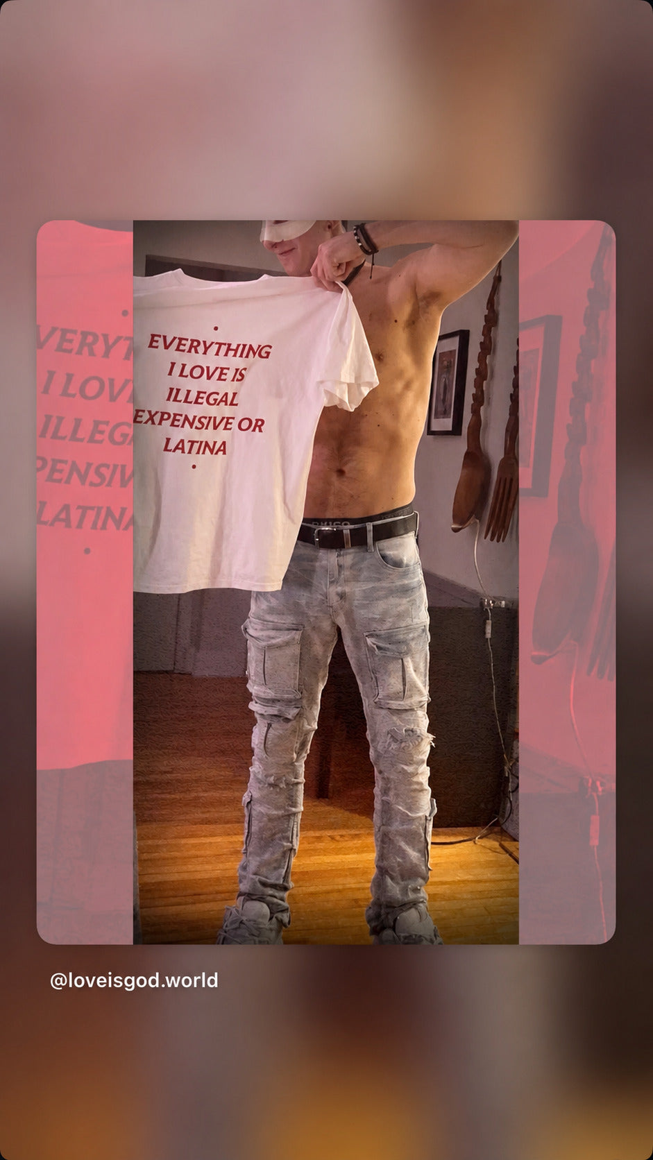 Mand holder en hvid EVERYTHING I LOVE IS ILLEGAL, EXPENSIVE OR LATINA T-shirt frem foran sig.