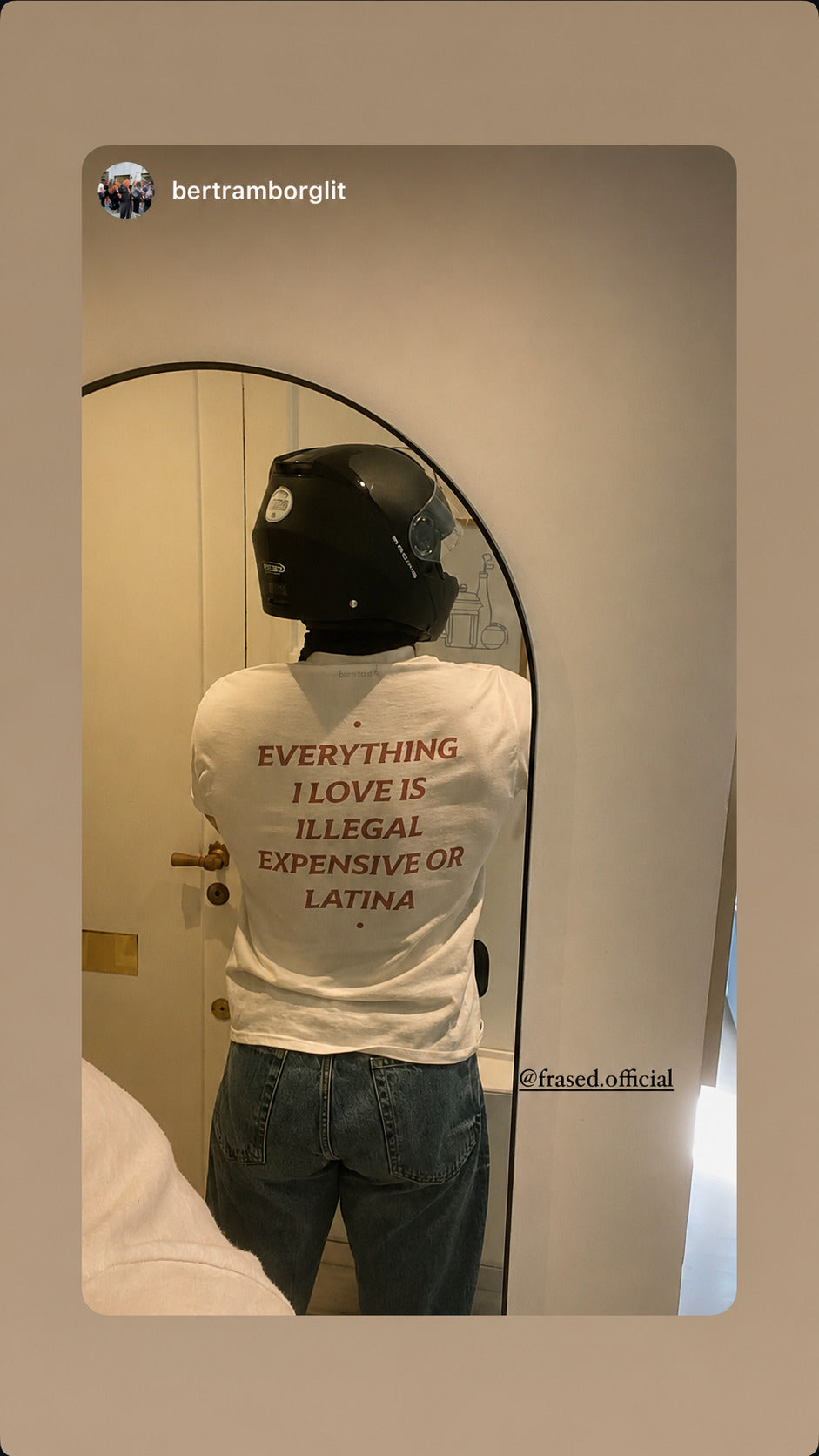 Person i hvid EVERYTHING I LOVE IS ILLEGAL, EXPENSIVE OR LATINA T-shirt og motorcykelhjelm foran et spejl.