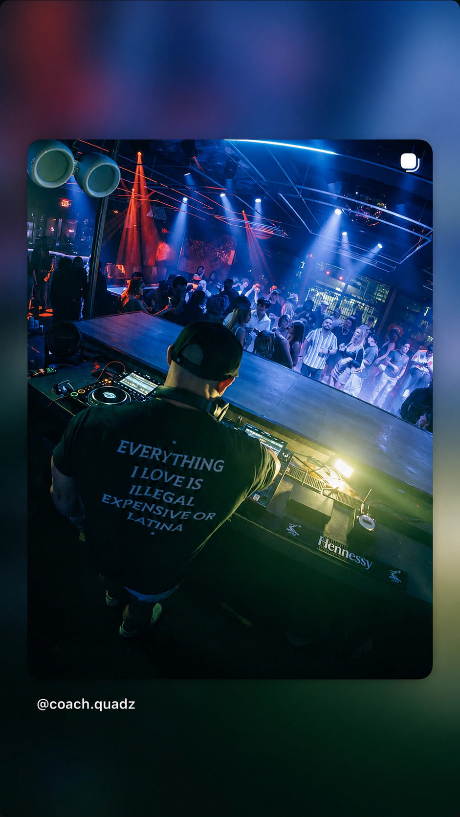 DJ i sort EVERYTHING I LOVE IS ILLEGAL, EXPENSIVE OR LATINA T-shirt foran et klubpublikum.