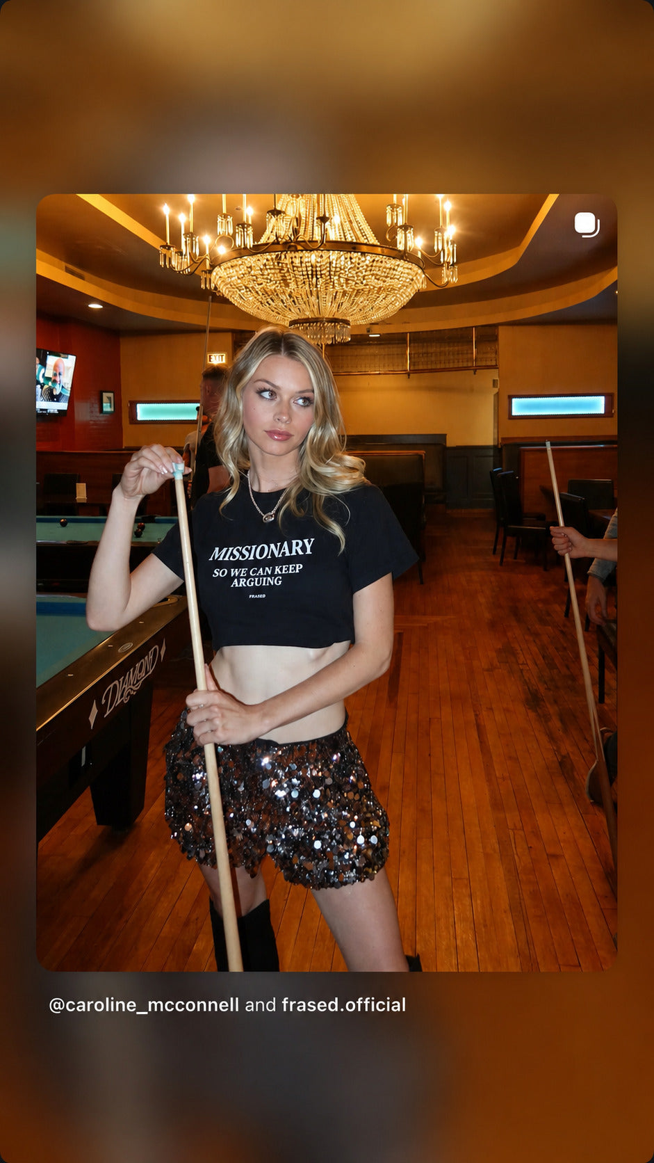 Woman by a pool table in a black FRASED baby tee with “Missionary So We Can Keep Arguing” on the chest.