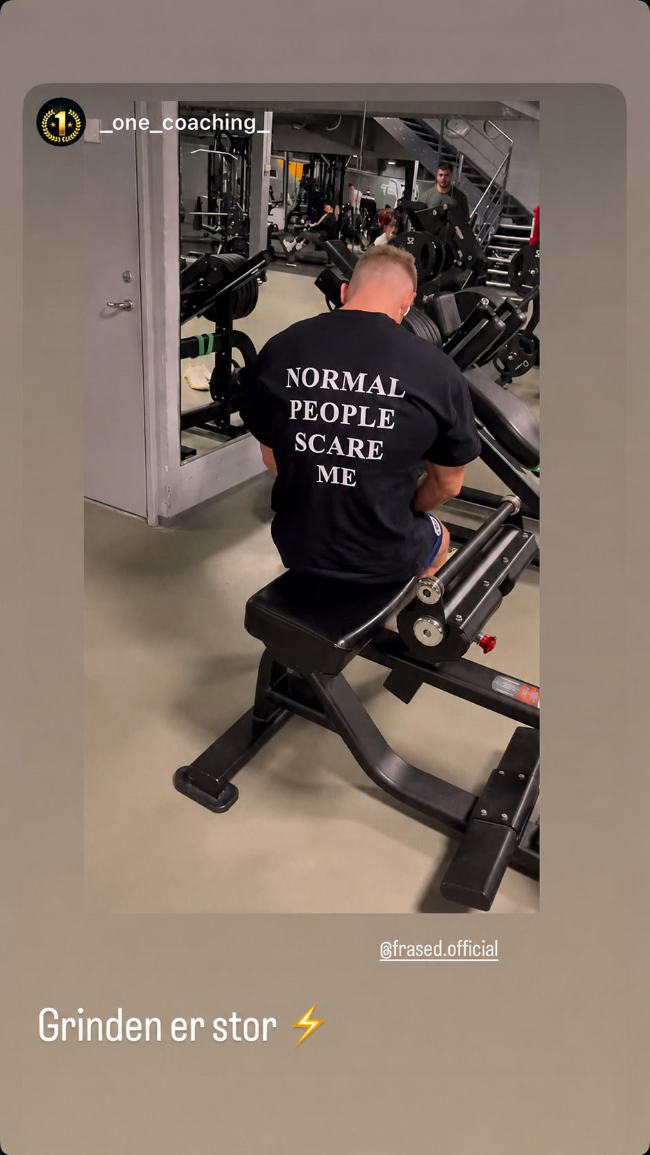 Mand i sort NORMAL PEOPLE SCARE ME T-shirt træner ved en maskine i fitnesscenter.