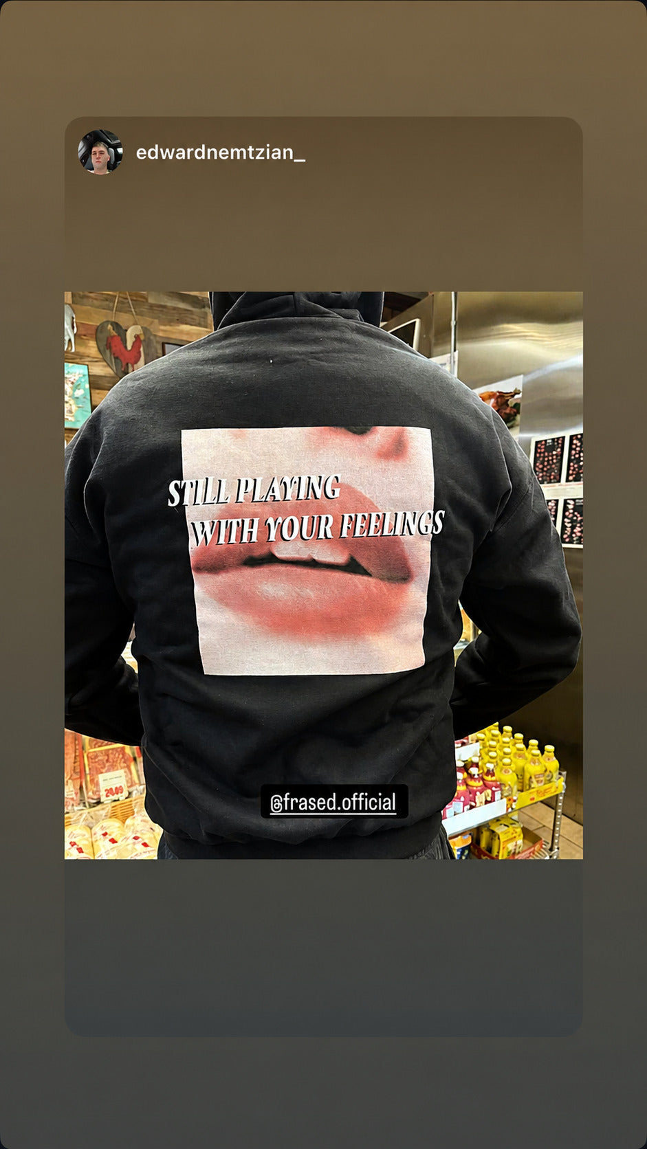 Person in a black “STILL PLAYING WITH YOUR FEELINGS” hoodie with a lip graphic standing in a shop.