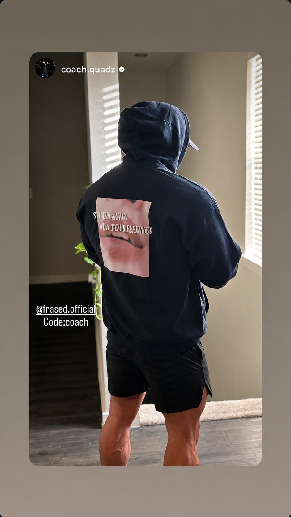 Person standing by a window in a black “STILL PLAYING WITH YOUR FEELINGS” hoodie.
