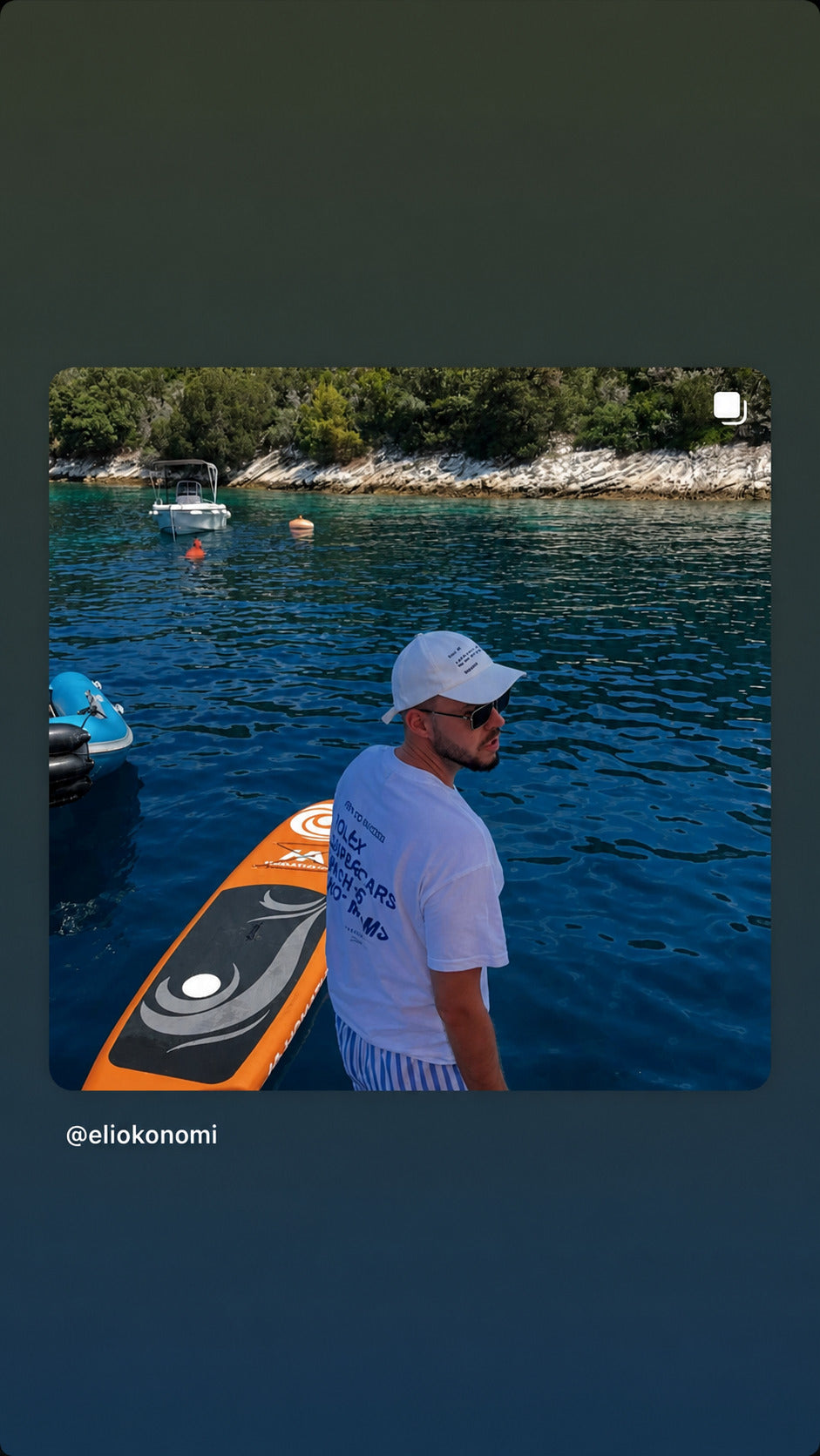 Mand ved vandet i hvid FRASED T-shirt med 'Here to succeed. Rolex Supercars Yachts Hot Moms' på ryggen.
