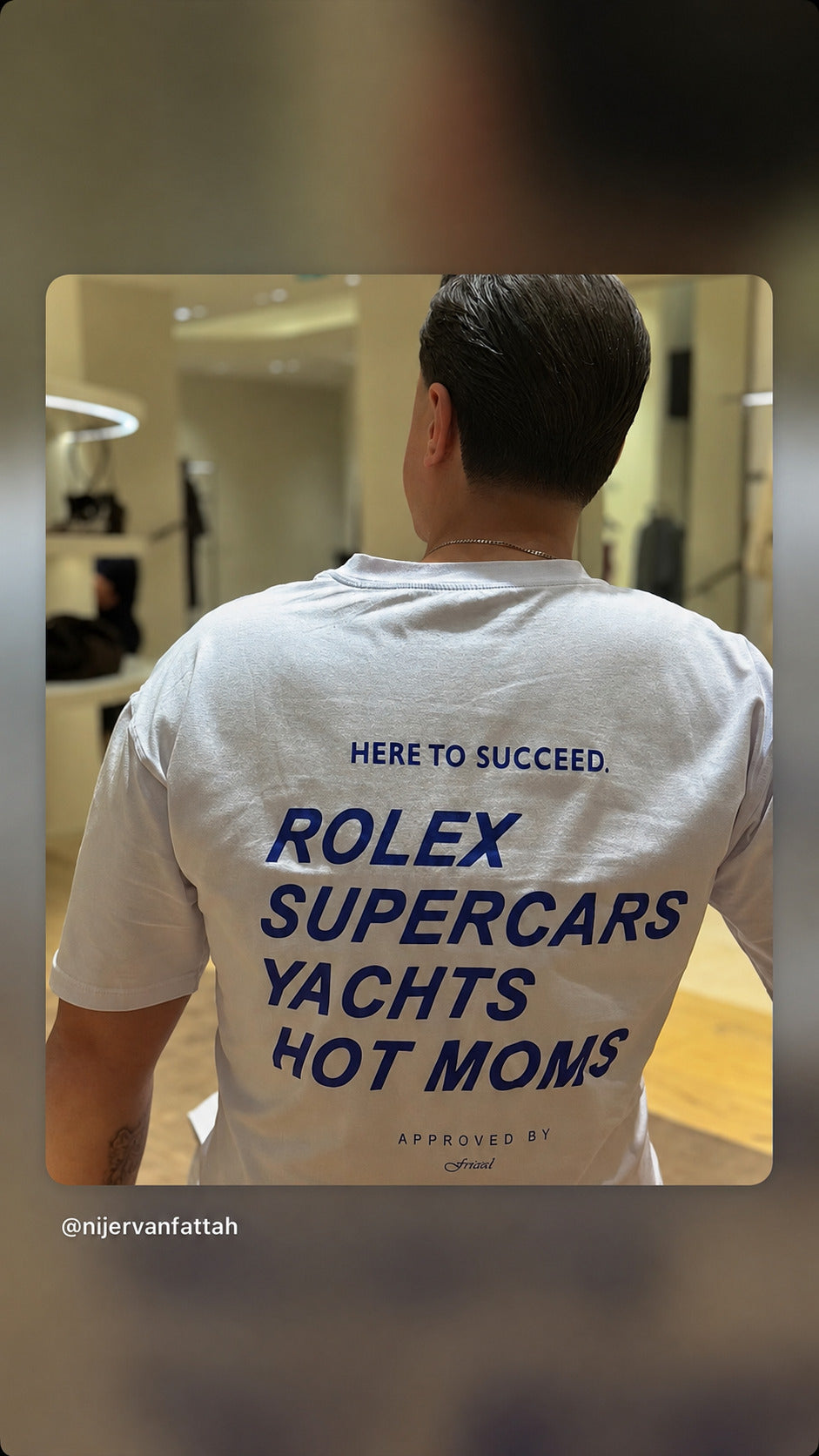 Mand set bagfra i hvid FRASED T-shirt med blåt 'Here to succeed. Rolex Supercars Yachts Hot Moms'-rygtryk.