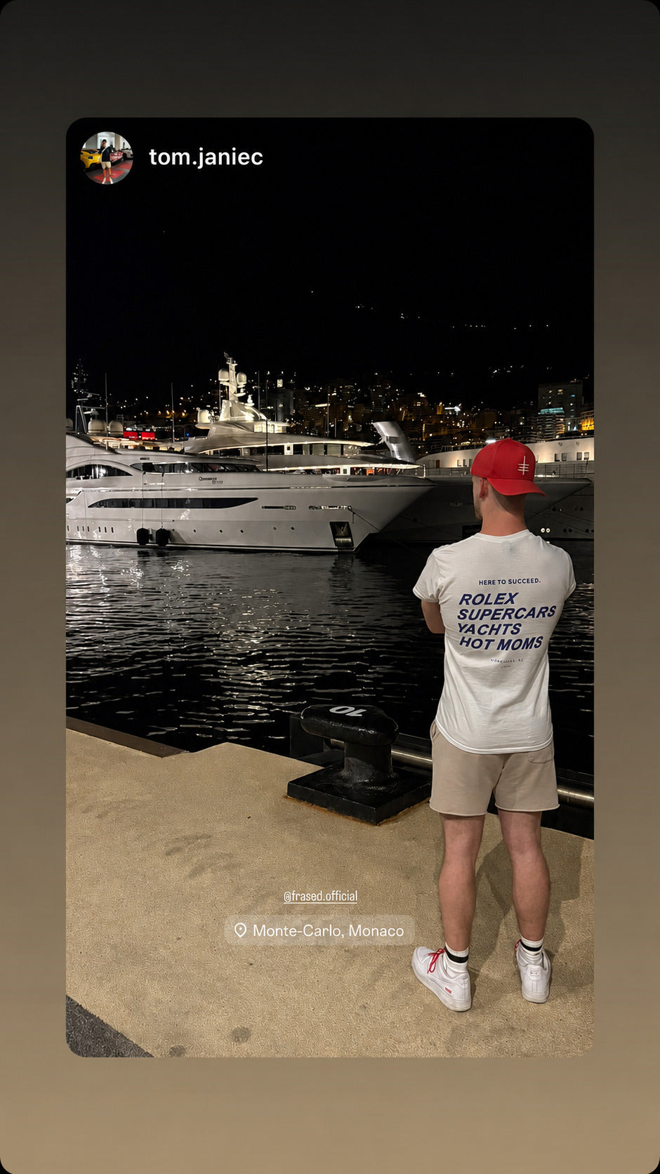 Mand ved lystbådehavn om aftenen i hvid FRASED T-shirt med 'Here to succeed. Rolex Supercars Yachts Hot Moms' på ryggen.