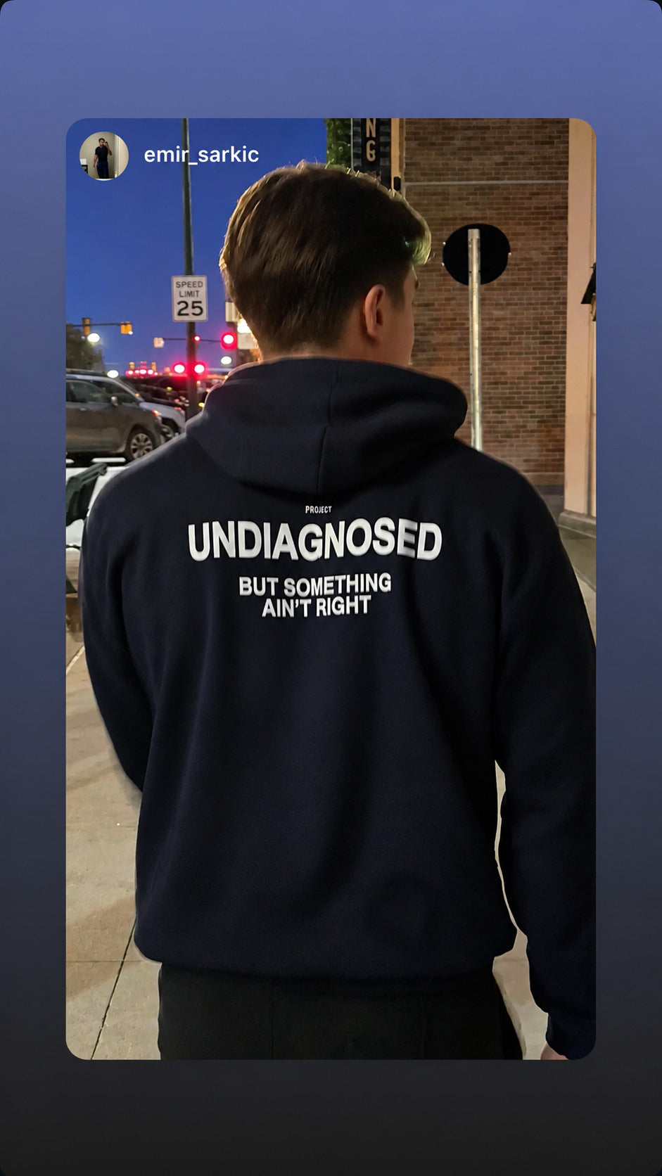 Person seen from behind on a pavement at night in a dark “UNDIAGNOSED” hoodie.