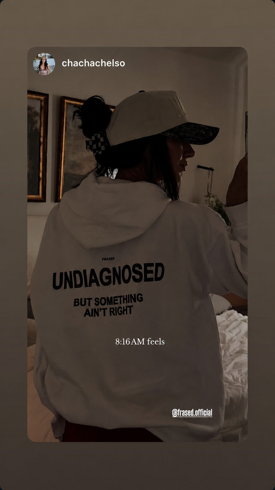 Woman seen from behind indoors wearing a white “UNDIAGNOSED” hoodie and a cap.