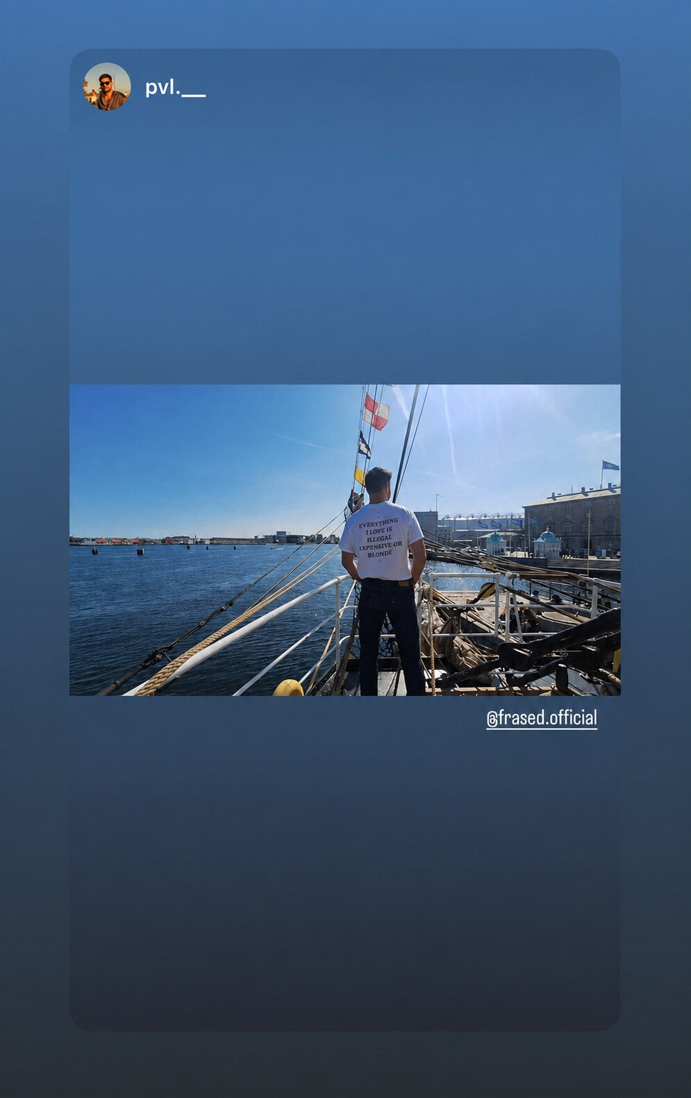 Man on a sailboat in a harbor wearing a white “EVERYTHING I LOVE IS ILLEGAL EXPENSIVE OR BLONDE” T-shirt.