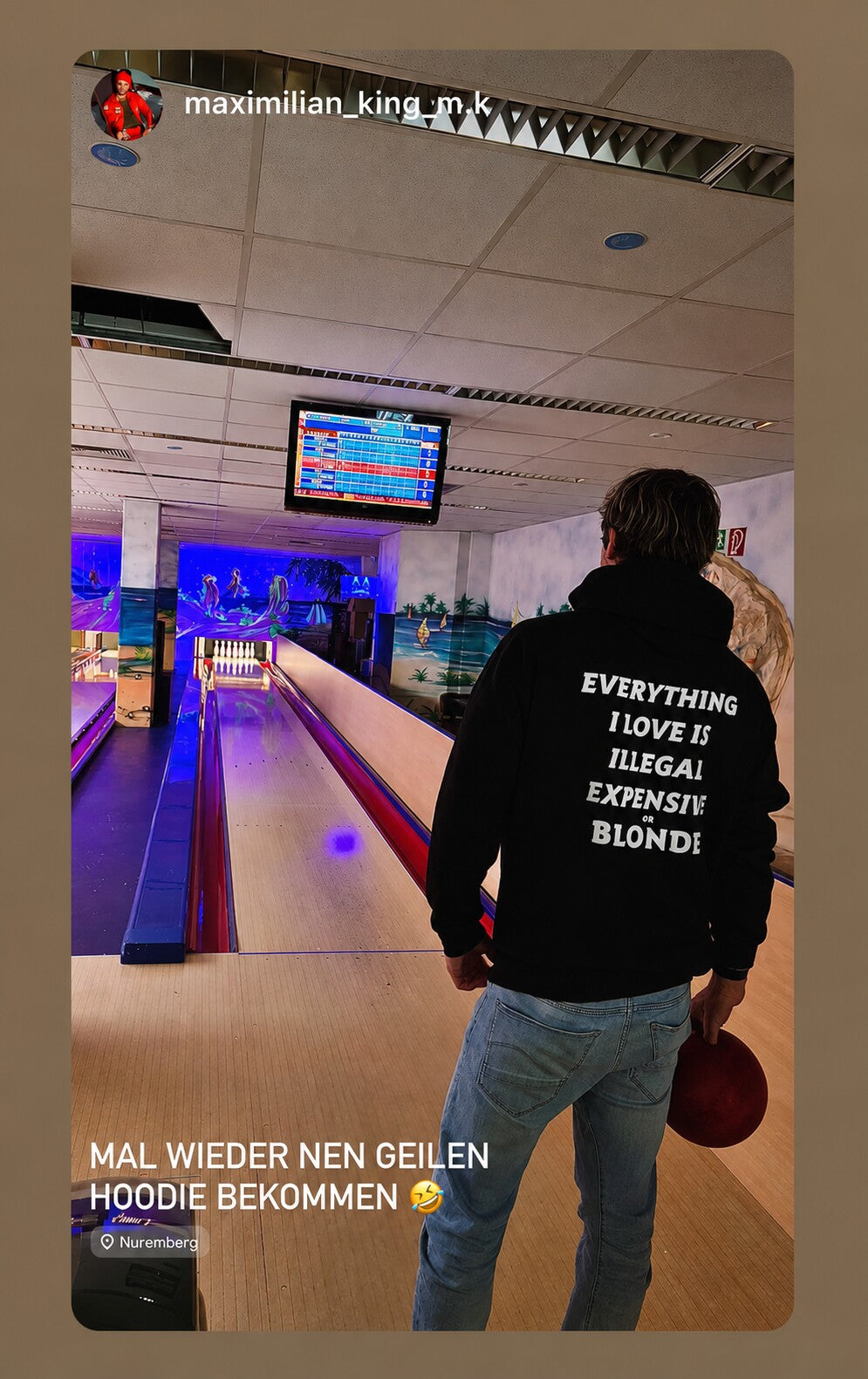 Man at a bowling alley in a black hoodie with white “EVERYTHING I LOVE IS ILLEGAL EXPENSIVE OR BLONDE” back print.
