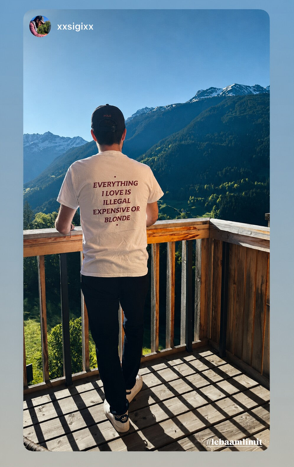 Person on a balcony overlooking mountains in a white “EVERYTHING I LOVE IS ILLEGAL EXPENSIVE OR BLONDE” T-shirt.