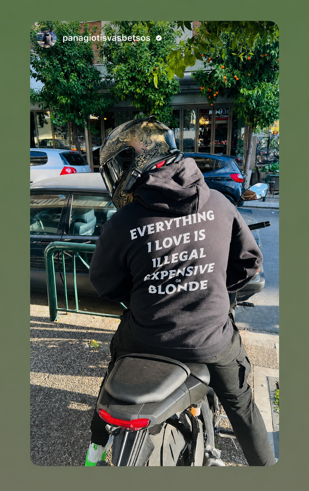 Motorcyclist on a parked bike in a black hoodie with white “EVERYTHING I LOVE IS ILLEGAL EXPENSIVE OR BLONDE” back print.