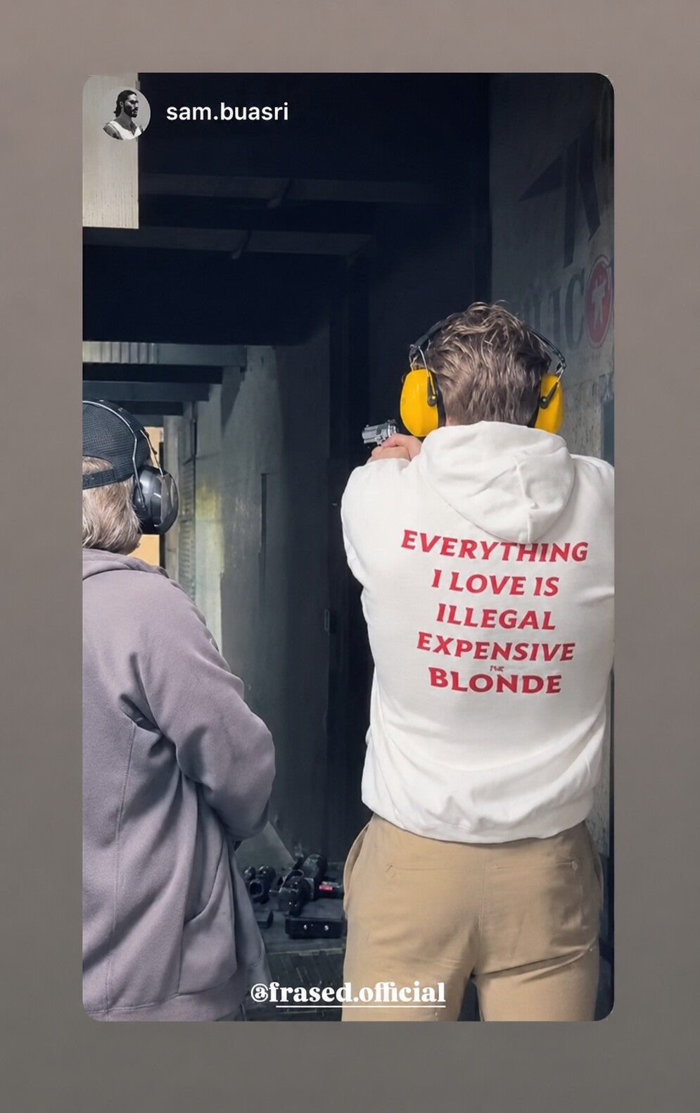 Person at a shooting range in a white hoodie with red “EVERYTHING I LOVE IS ILLEGAL EXPENSIVE OR BLONDE” back print.