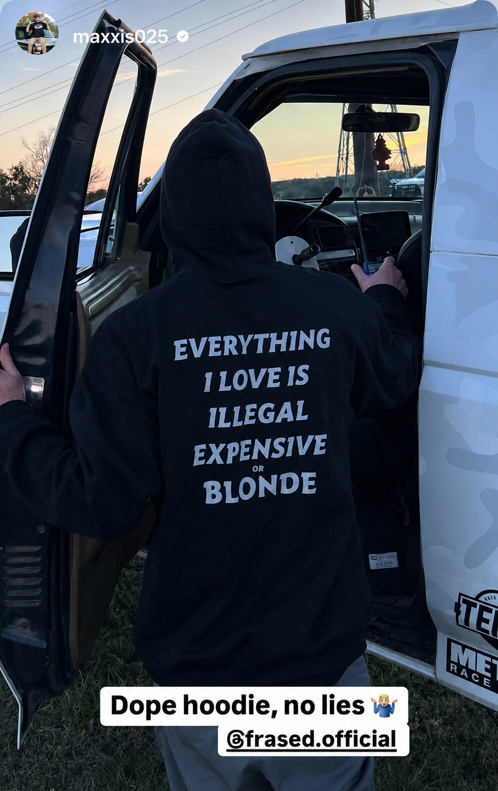 Person beside an open car door in a black hoodie with white “EVERYTHING I LOVE IS ILLEGAL EXPENSIVE OR BLONDE” back print.