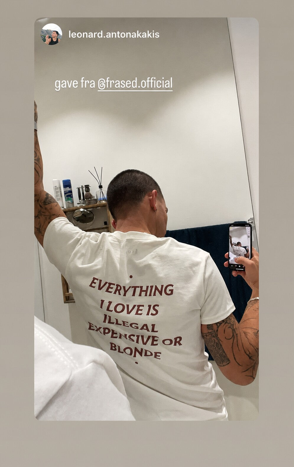 Man taking a mirror selfie in a white “EVERYTHING I LOVE IS ILLEGAL EXPENSIVE OR BLONDE” T-shirt.