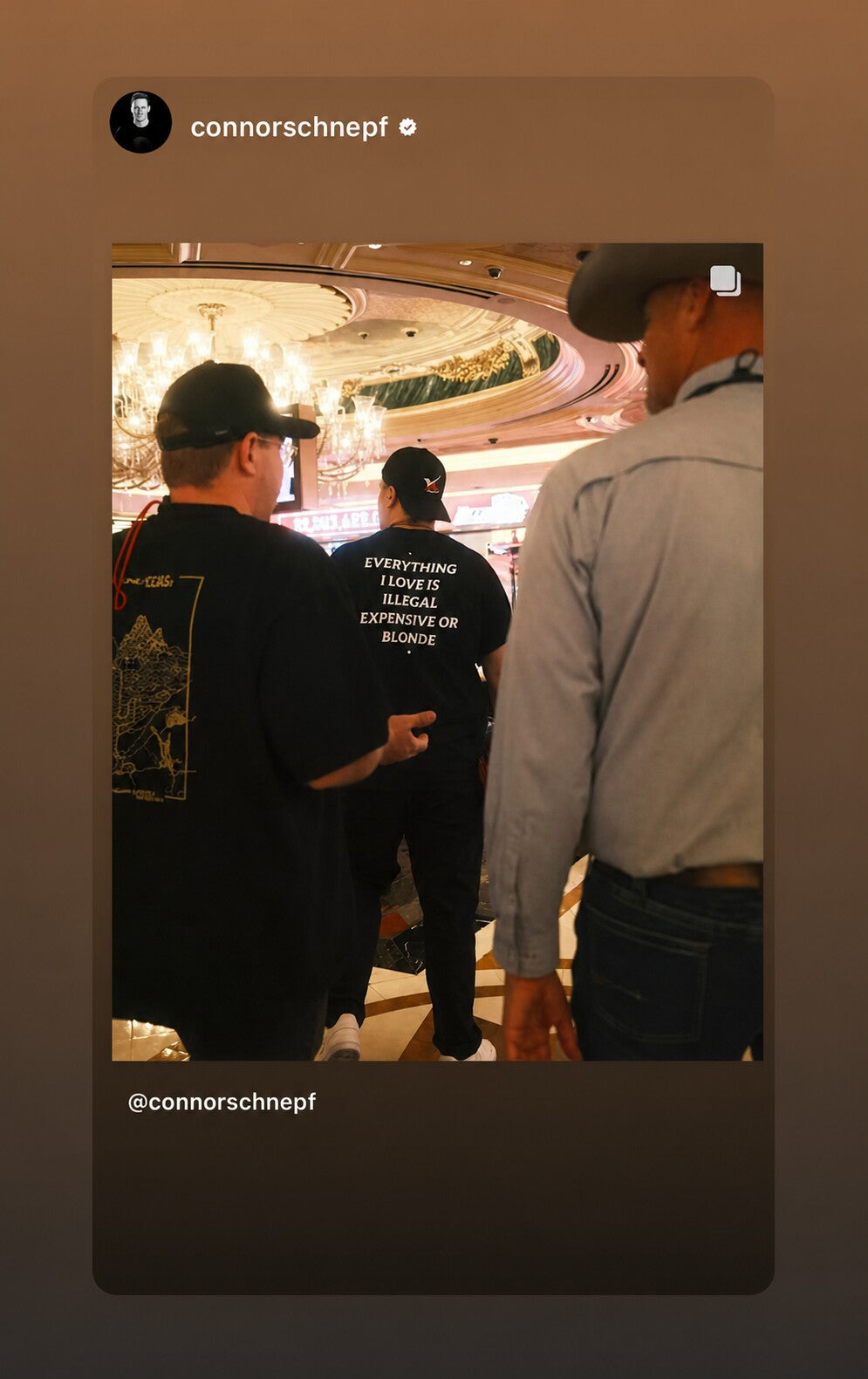 Person in a lobby wearing a black “EVERYTHING I LOVE IS ILLEGAL EXPENSIVE OR BLONDE” T-shirt.