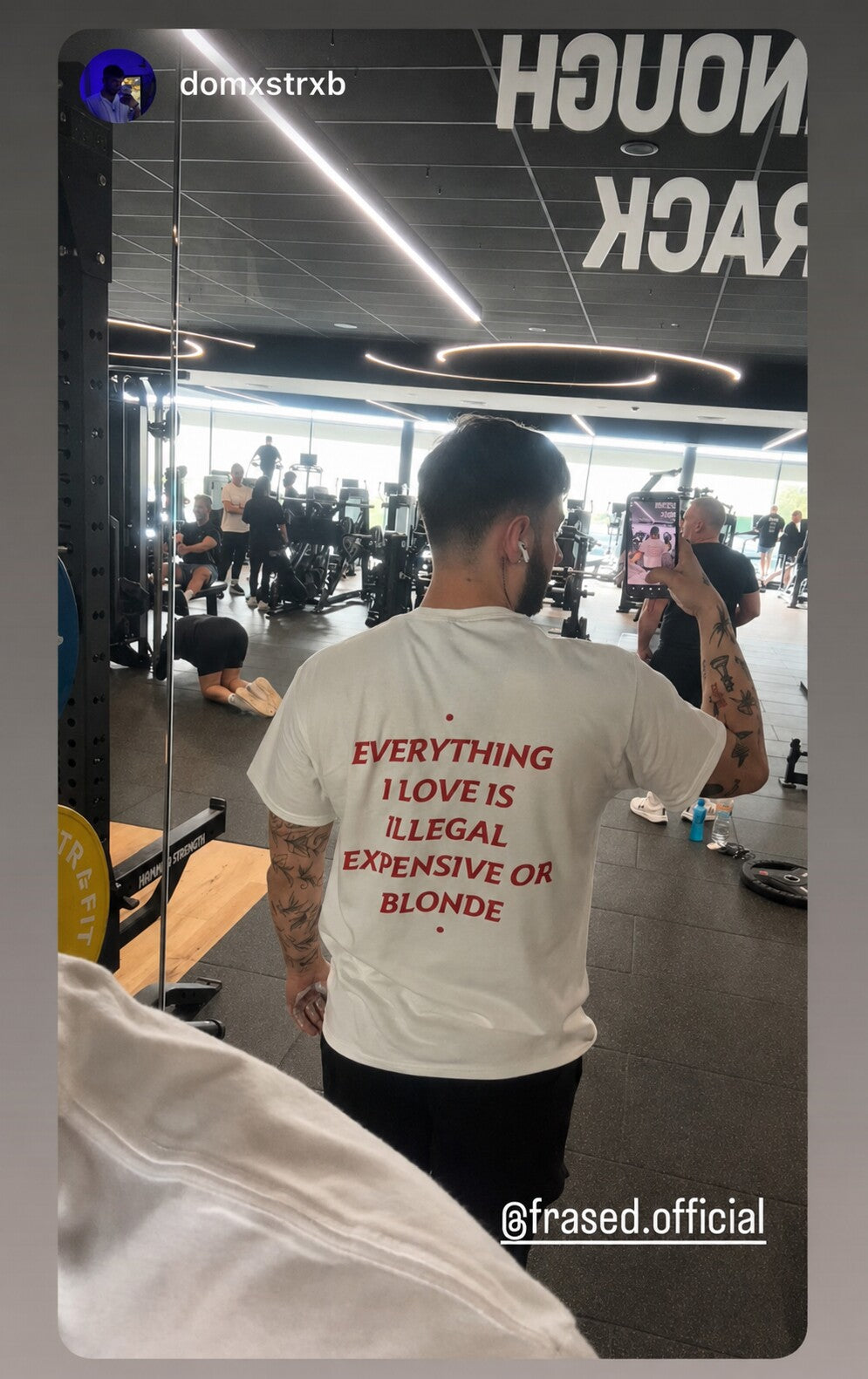Man taking a gym mirror selfie in a white “EVERYTHING I LOVE IS ILLEGAL EXPENSIVE OR BLONDE” T-shirt.